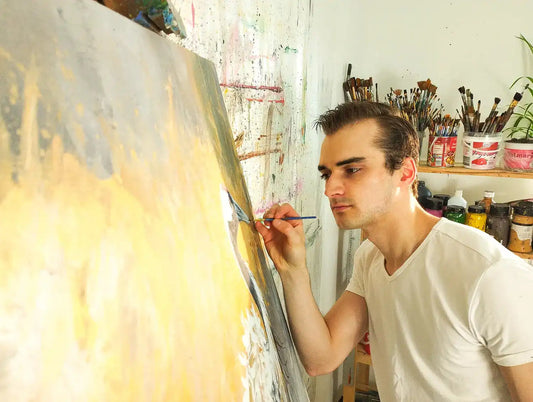 Daniel Heinz (danh1z) malt im Atelier an einem großen, expressiven Acrylgemälde mit gelb-grauen Farben.