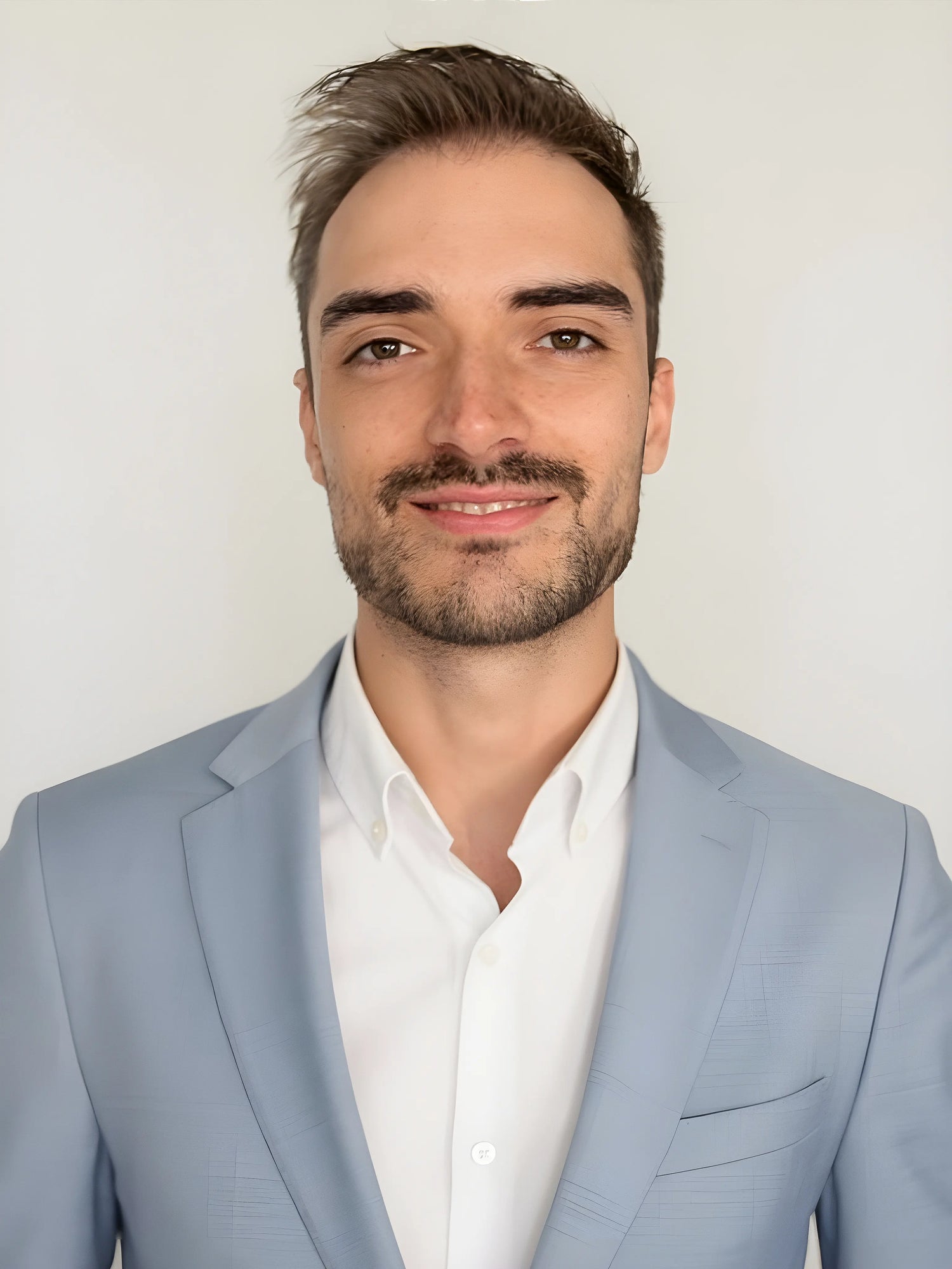 Porträtfoto des Künstlers Daniel Heinz, lächelnd in hellblauem Sakko und weißem Hemd vor neutralem Hintergrund.